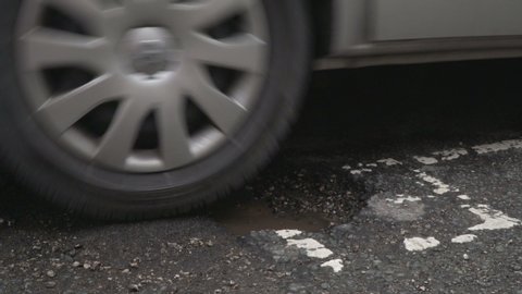 Van tyre driving over a Pothole damaged road which is covered in Potholes in the street.  Sideways view