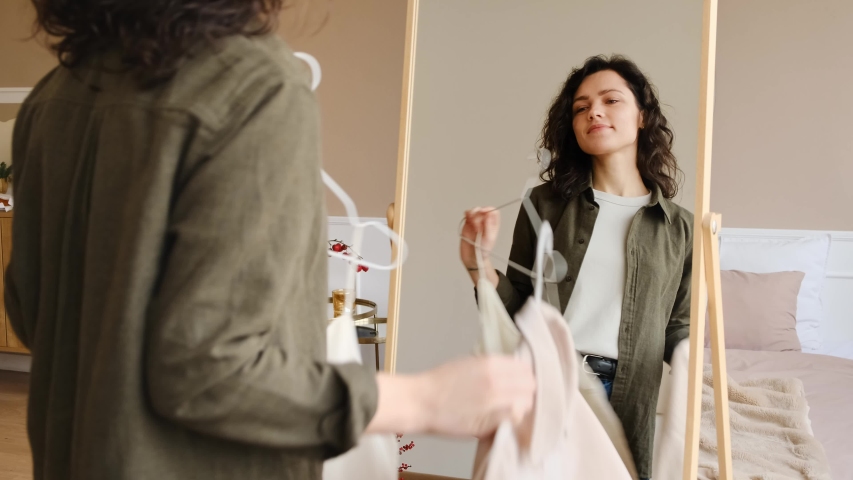 A young woman is going to a meeting, chooses clothes in front of a mirror. Hard choice routine of what clothes to wear. Getting dressed. | Shutterstock HD Video #1044201190