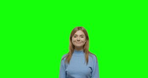 Young cheerful woman pointing to side and upwards with both hands showing object in copy space against green screen background . Girl having fun on Chroma Key. 4k video footage slow motion 60 fps