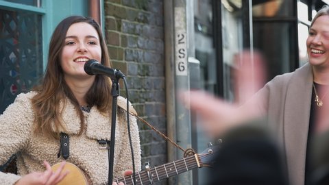 Young woman busking playing acoustic guitar and singing outdoors to applauding crowd in street - shot in slow motion