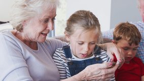 Grandmother at home with grandchildren having fun playing video game on mobile phone - shot in slow motion