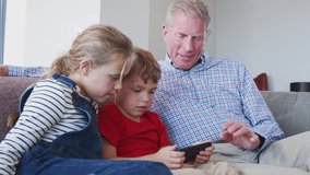 Grandfather at home with grandchildren having fun playing video game on mobile phone - shot in slow motion