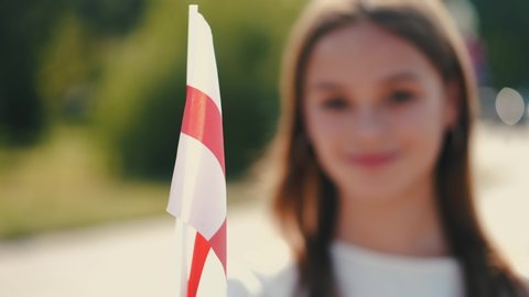 A student is waving flag of England on a stick. She is at the park square.