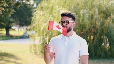 A young man is waving the flag of Canada. The boy is smiling and standing at the park.