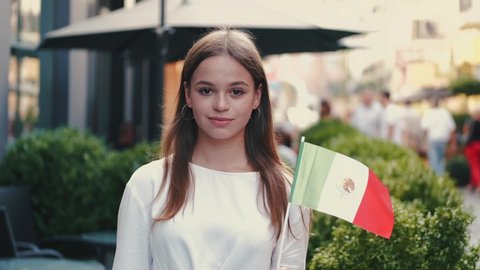 A student is waving Mexican flag on a stick.There is a cafe at the background.