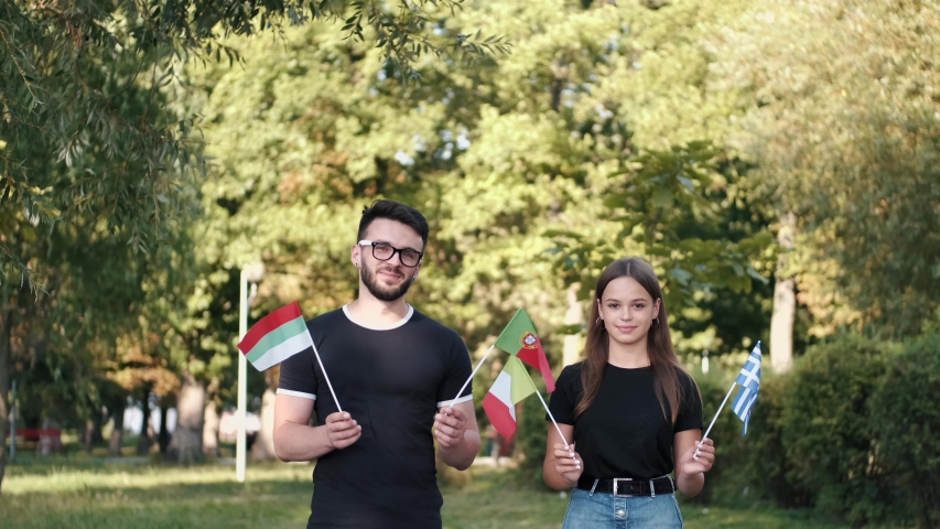 Two young persons are showing different flags of the countries. The Greek, Bulgarian, Portuguese and Italian flags are waved.