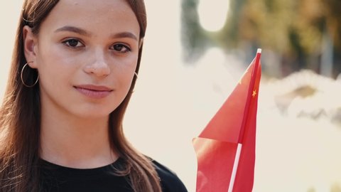 A young lady is showing the national flag of China on a stick.The flag is waving against the fountains.