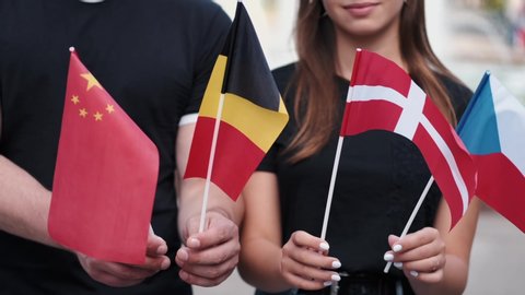 A boy and a girl are showing different flags of the countries. The students are waving Belgian, Danish, Chinese and Czech national flags.