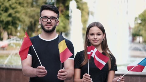 A boy and a girl are showing different flags of the countries. The students are waving Belgian, Danish, Chinese and Czech national flags.