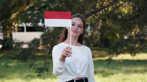 A student is waving the flag of Poland on a stick. The girl is at the park.