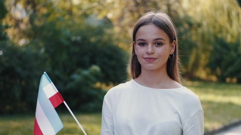 A young European lady is waving the Hungarian flag. She is at the park.