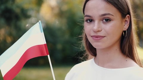 A young European lady is waving the Hungarian flag. She is at the park.