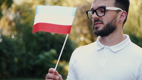 A young European man is waving the Hungarian flag. There is nature at the background.