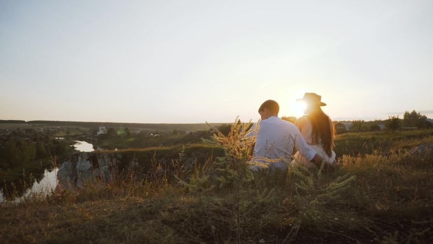 Unrecognizable couple is watching sunset on the cliff. Romantic scene of boyfriend hugging girlfriend looking at horizon. Beloved lovers spend summer holidays outdoors