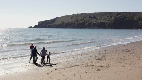 Drone shot of multi-generation family walking along shoreline of beach by breaking waves