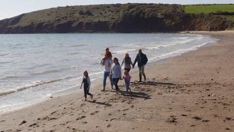 Drone shot of multi-generation family walking along shoreline of beach by breaking waves