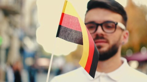 A student is waving German flag on a stick. The boy is on the street.
