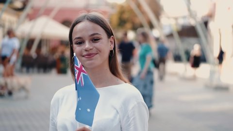 A young lady is waving Australian flag on a stick. The girl is on the street.