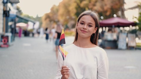 A student is waving German flag on a stick. The girl is on the street.
