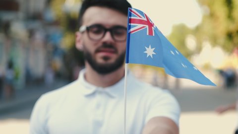 A young man is waving Australian flag on a stick. He is on the street.