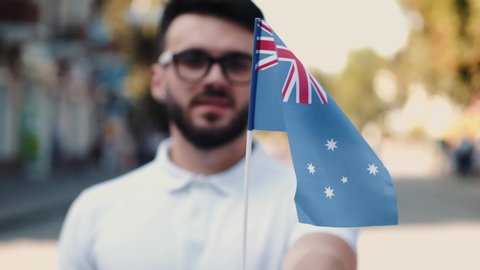 A young man is waving Australian flag on a stick. He is on the street.