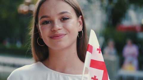 European student is waving the flag of Georgia. The girl is smiling.