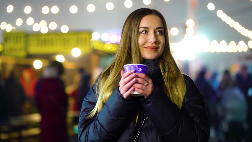 Attractive girl with hot drink in winter with illumination on background