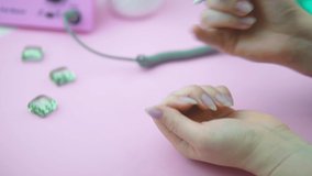 A woman removes gel polish from a nail. Removing the gel coating with a manicure machine. Modern hardware manicure. Video on the topic of beauty and nail care. Manicure accessories. High quality, 4K.