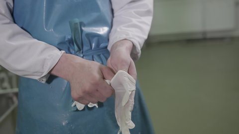 Guy in special clothes puts on white gloves in a sausage factory