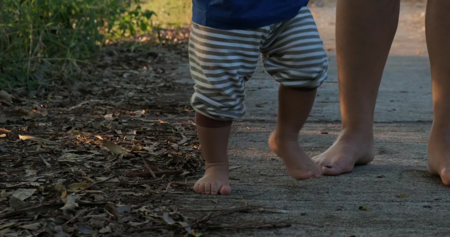 Boy firrst walking practice on nature road teach with mom leg close up slow motion baby developement concept