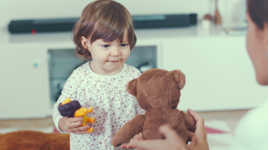 Portrait of cute little one year old girl laughing happily while playing and hugging with her mother at home with a teddy bear. Shot in 6k, cine lens. Instagram style. Royalty-Free Stock Footage #1044254245