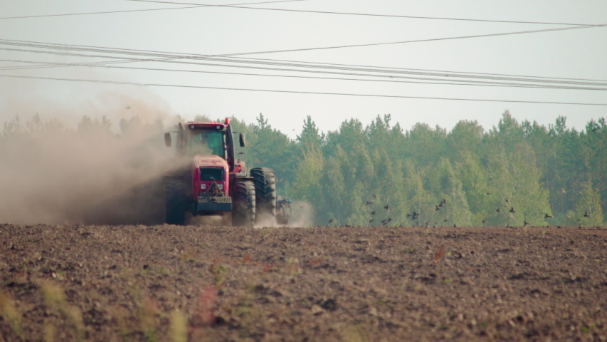 Front view of a farmer on a red tractor plowing the dusty arid soil. The farm car is followed by hungry birds. Agribusiness in the spring Royalty-Free Stock Footage #1044254374