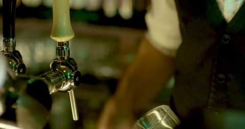 Vintage elegant barman, pouring a blonde beer with skill. Close Up shot inside a pub. Vintage bar in a cold light