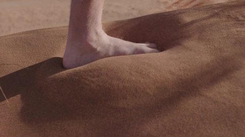Slow motion shot of feet walking on the red sand of a dune in the Namib desert.