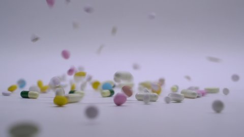Huge number of different kinds pills falling on white background in slow motion. Multi-colored tablets are flying. Beautiful drop pills on table. medical footages, healthy lifestyle, vitamins, drugs