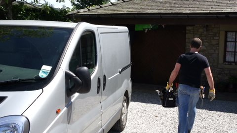 Tradesman gets tool box out of his van. The handyman is outside, wearing a tool belt as he gets to his vehicle
