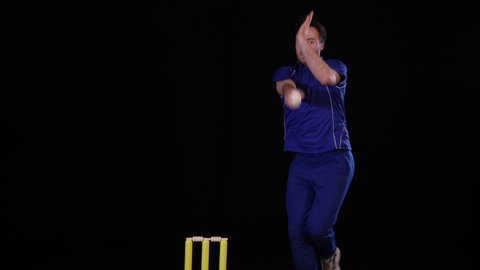 Cricket Bowler bowling the ball in a game of the sport- Black background. Dressed in blue. TwentyTwenty