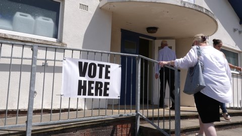 Vote here Sign - Man & Woman  walking past and going to vote in the election. Politics. Slow motion  -4K Stock Video clip footage