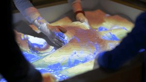 Augmented reality sand box, close up with adult and children playing with the sand.  Science demonstration teaches hands on topography and mapping.  Interactive learning, fun demonstration. - Powered by Shutterstock - Get 15% off with code: PIKWIZARD15