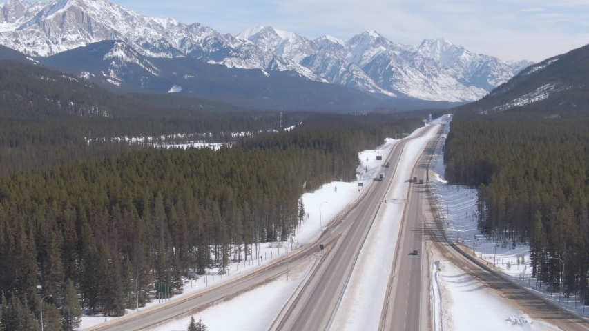 DRONE: Cargo truck hauls a heavy trailer down the scenic Trans Canada Highway. Freight lorries transport heavy cargo across the picturesque landscape with snowy mountains and lush green forests.