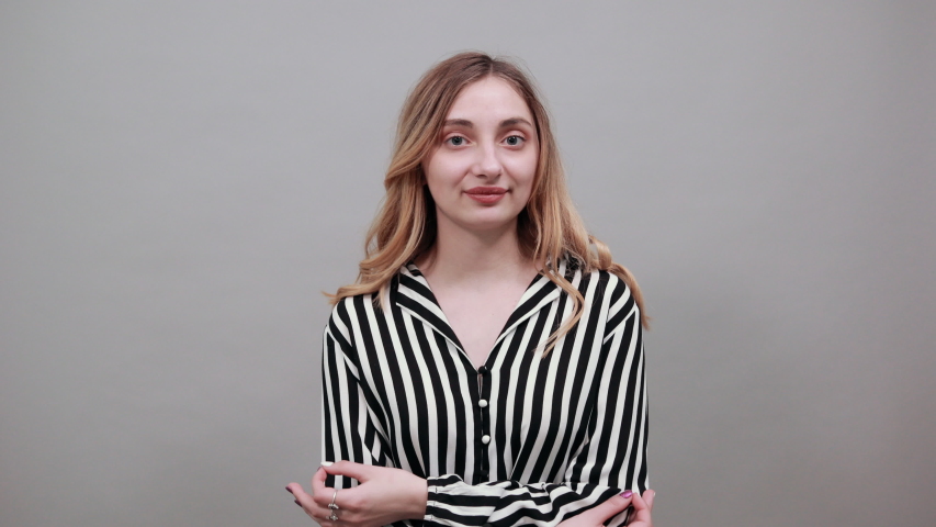 Calm caucasian woman in fashion black and white striped shirt looking down, praying, keeping hands together isolated on gray background in studio. People sincere emotions, lifestyle concept.