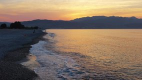 Aerial low-altitude video from drone on Platanias beachfront area, beach and sea at sunset time. Rodopos peninsula is on background. Chania prefecture, Crete, Greece. 