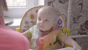 Young woman tease with a cookie her beautiful little son at the table and baby boy watching into the camera and then take the cookie and trying to feed his mother close up view slow mo video in 4K