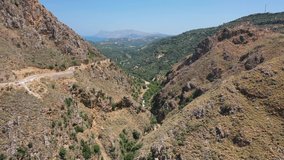 Aerial bird's-eye view video from drone of flight from Topolia Gorge canyon to a mountain valley with olive groves and mountain Topolia village. Kissamos, Chania prefecture, Crete, Greece.