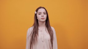 Charming young woman looking at camera, keeping fingers crossed, make wish wearing fashion pastel shirt isolated on orange background in studio. People sincere emotions, lifestyle concept.