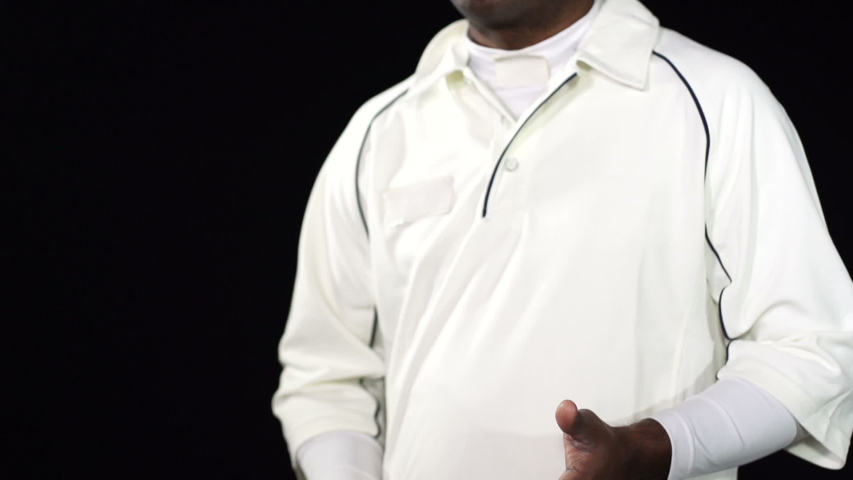 Cricket Bowler waiting to bowl the ball in a game of the sport- Black background. Dressed in white. He spins the ball to himself.