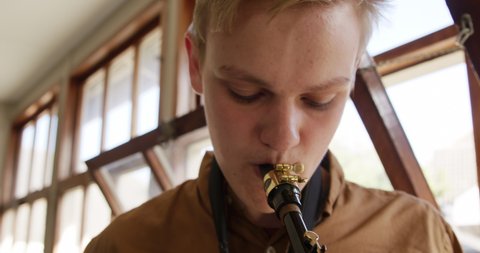 Front view close up of a teenage musician boy standing playing a saxophone during a school band practice. He is focused