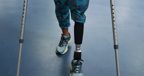 Front view of a Caucasian woman with a prosthetic leg walking on crutches at a sports centre gym to make improvement 