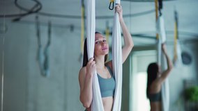 Waist up video portrait of fit young woman looking in camera and smiling while standing on hanging hammock in aerial yoga studio