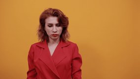 Serious caucasian young woman keeping hand on chin, looking up, thinking about issue wearing fashion red jacket over isolated orange background. People lifestyle concept.